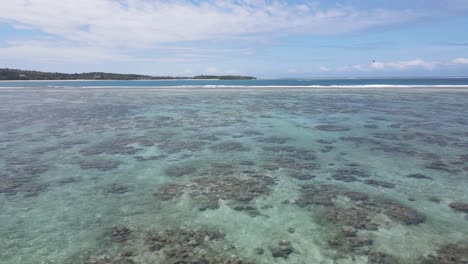 Drone-panoramic-view-sweeps-over-the-glistening-waters-of-Natadola-Beach-,-revealing-intricate-coral-formations-beneath-the-surface