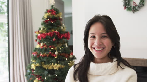 portrait of happy biracial woman smiling by christmas tree at home, copy space, slow motion