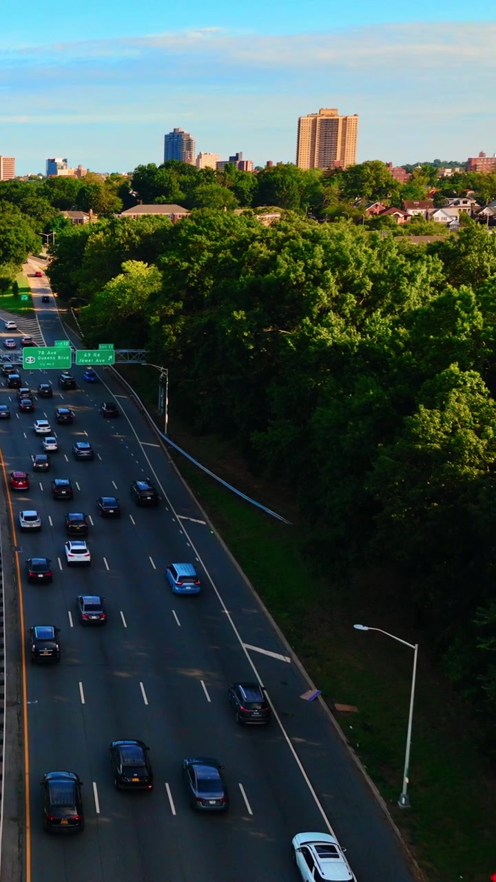 Autostrada sopraelevata fiancheggiata da alberi, Queens, New York. Prospettiva dall'alto del traffico su più corsie, di un segnale stradale e di torri residenziali lungo l'orizzonte. Video verticale.