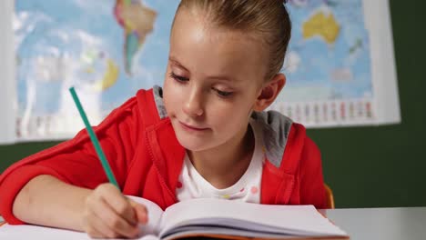 schoolgirl doing homework in classroom at school