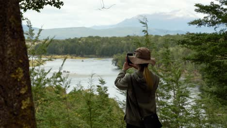 Female-hiker-walks-out-to-take-photo-of-grand-New-Zealand-landscape-on-the-Kepler-Track,-overcast-even-lighting-in-sky