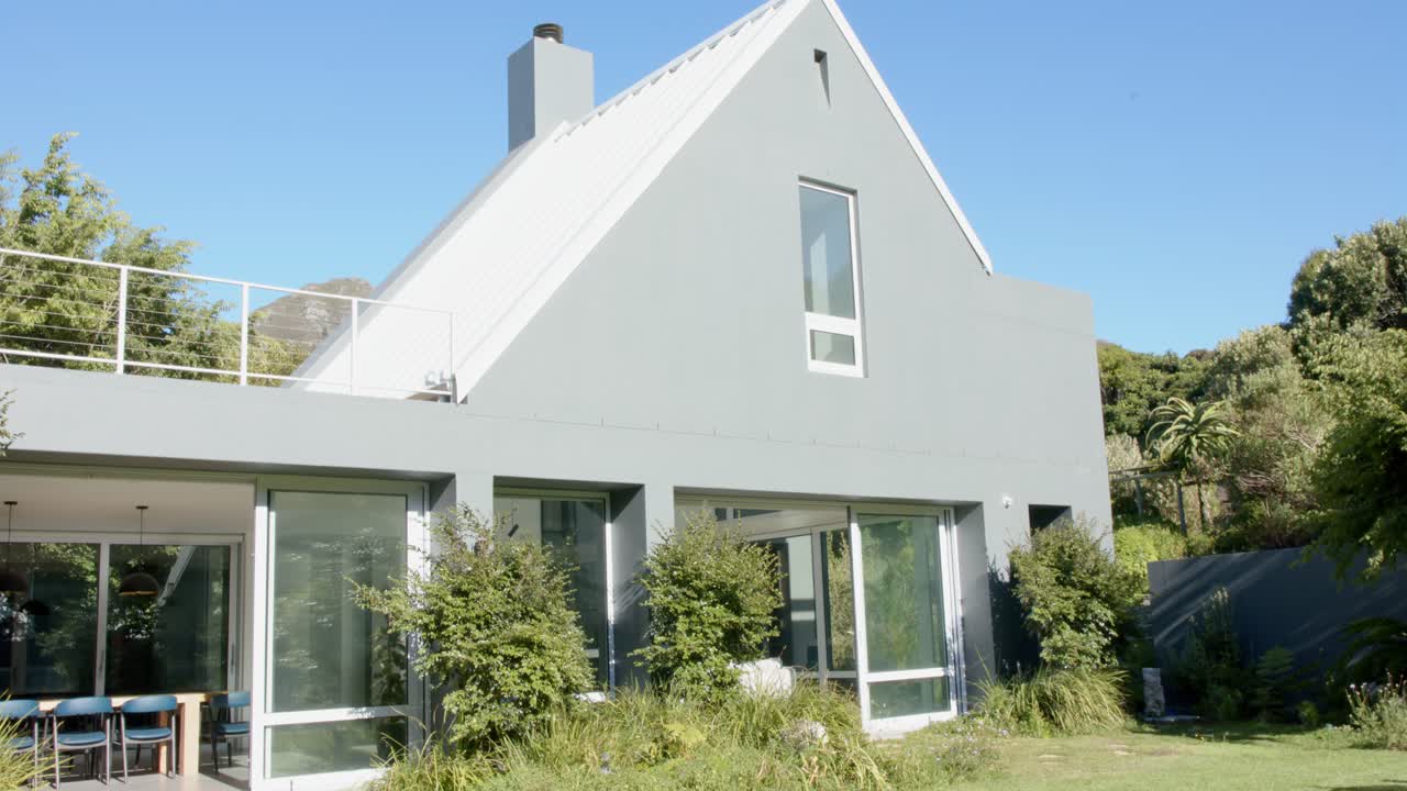 Kameraet trækker sig tilbage og viser et to-etagers hus med stejl gavl, altan, glasdøre og græsplæne