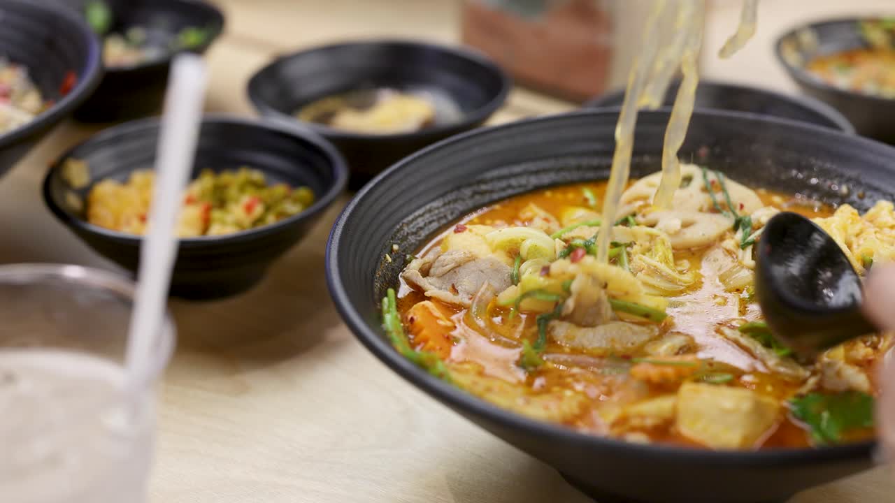Hand uses chopsticks to lift noodles from vibrant spicy hotpot in warmly lit restaurant setting