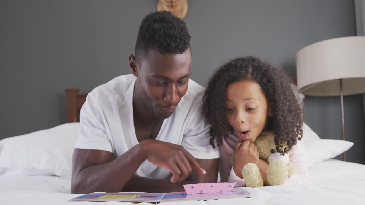 African american father reading a story to his daughter in bed