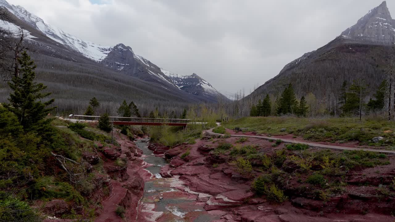 Torrente di Red Rock Canyon che scorre sotto un ponte con montagne e foreste nel Parco Nazionale dei Laghi Waterton, Canada