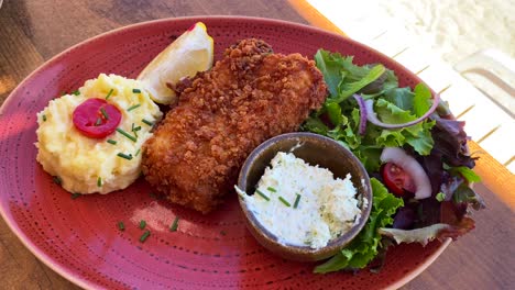 delicious deep-fried fish with mashed potatoes and salad on a red plate, seafood, 4k shot