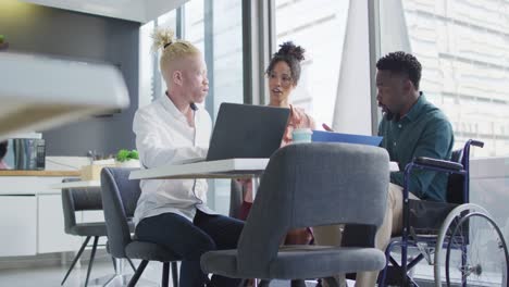 Diverse-business-people-discussing-with-disabled-colleague-and-documents-in-creative-office