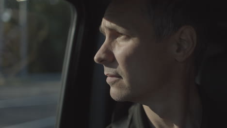 an adult male riding passenger side in a car stares out the window