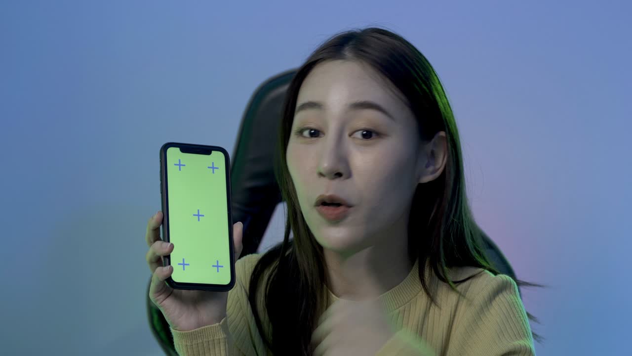 젊은 여성 게이머가 그녀의 증기 방에서 카메라와 대화합니다. 그녀는 스마트폰을 보여주고 카메라에 이야기합니다.