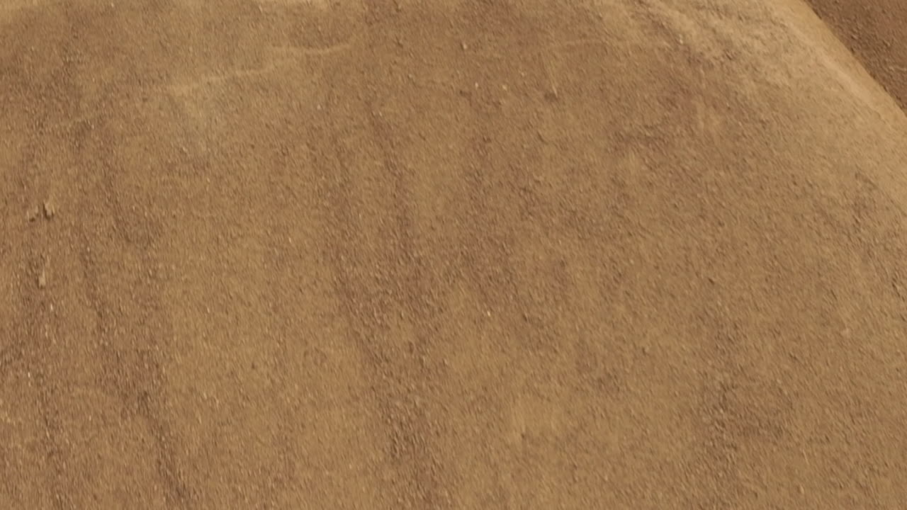 발굴 현장에서 많은 양의 모래를 움직이는 초록색 기계 팔의 근접 공중 사진