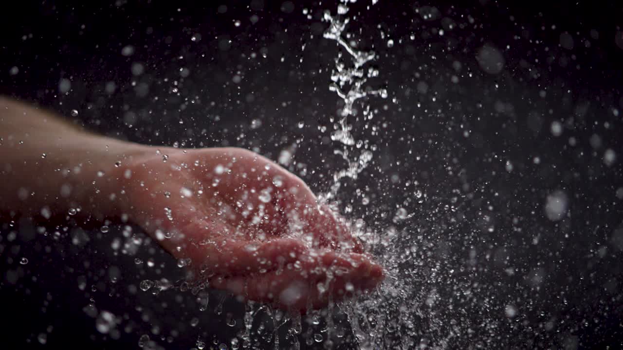 인간 손이 떨어지는 물방울을 초 느린 동작으로 잡고, 검은 바탕, 생생한 세부 사항