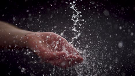 Human-hand-catching-falling-water-drops-in-a-super-slow-motion,-black-background,-vivid-detail