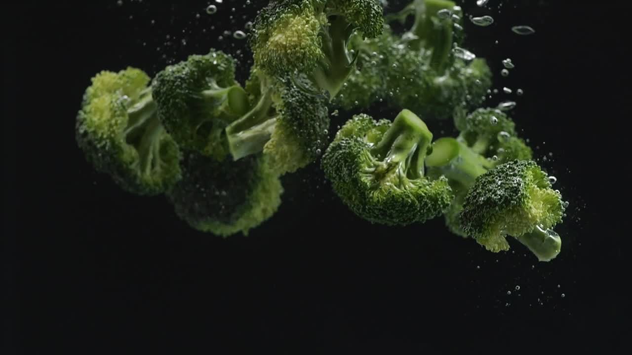 Many Broccoli Falling Into Water On The Black Background