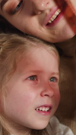 blonde little girl chooses shot to print on processed coloured film roll with happy mother lying on sofa at home close view slow motion