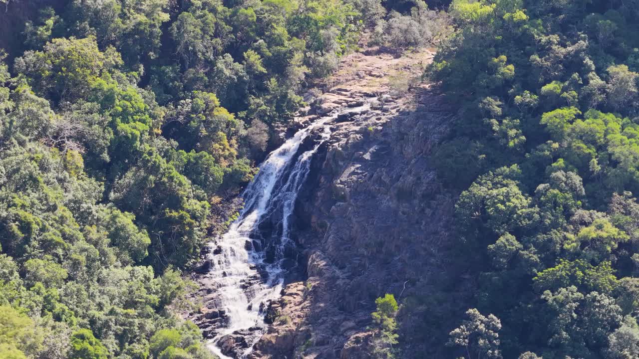 Drone footage captures a cascading waterfall amidst lush greenery in Port Douglas, Australia, with dynamic camera movement and natural lighting
