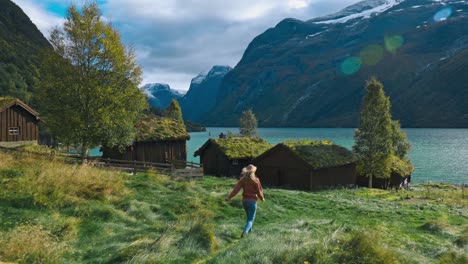 Camera-following-a-girl-running-and-walking-towards-abandoned-houses,-covered-in-grass-and-moss