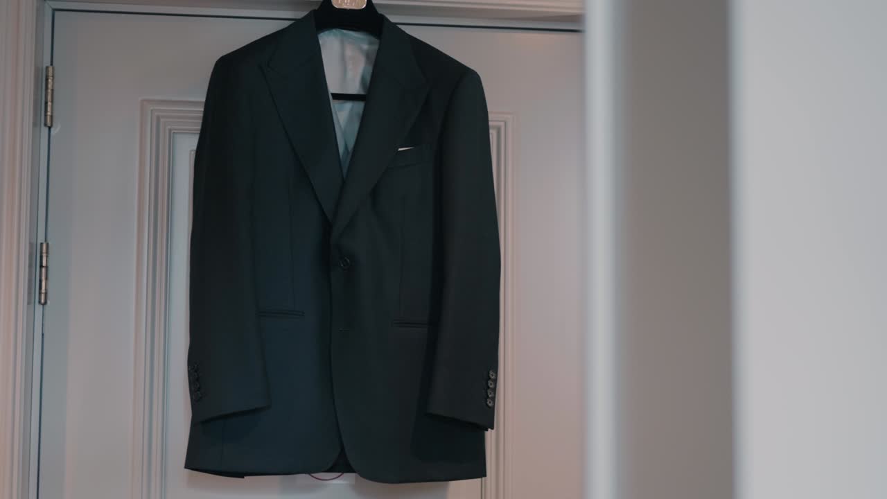 elegant men’s blazer hangs centered on white door in soft natural light