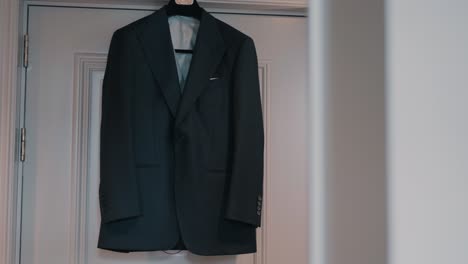 elegant men’s blazer hangs centered on white door in soft natural light