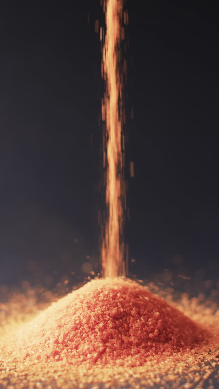 Vertical video of close up of heap of red sand grains and copy space on black background