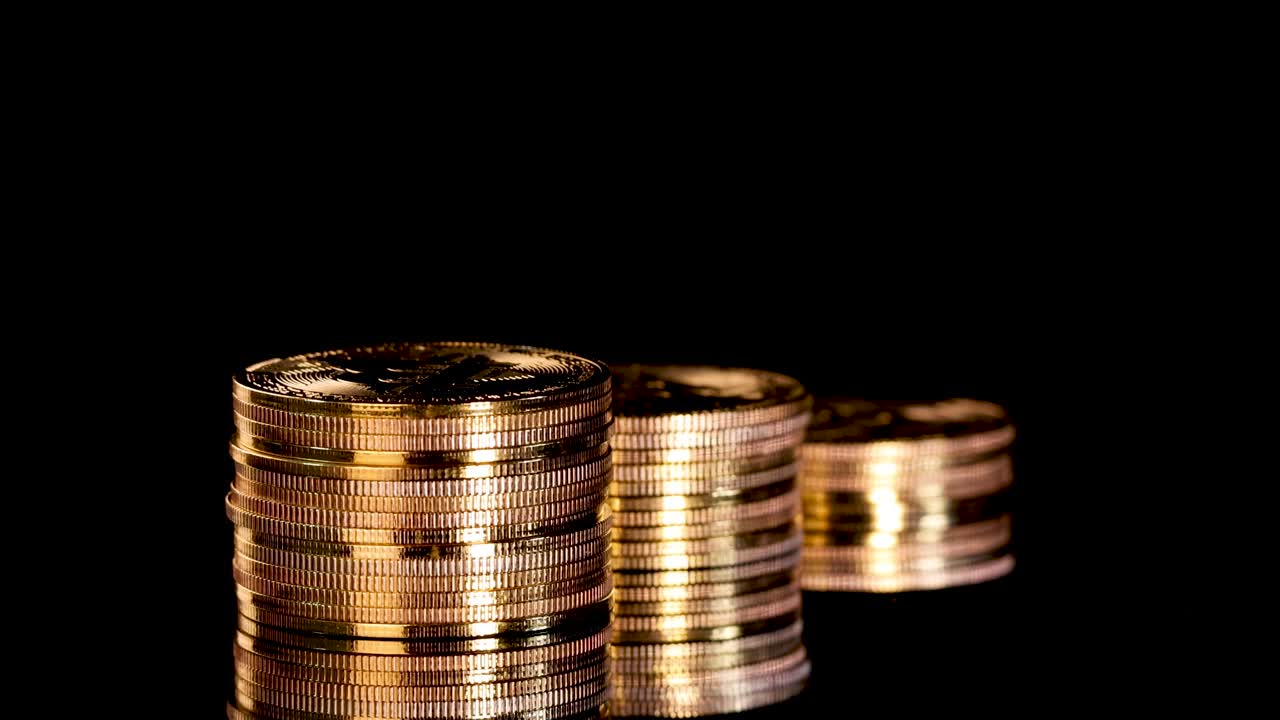 Three gold coin stacks rotate smoothly, illuminated by dramatic lighting against a black background