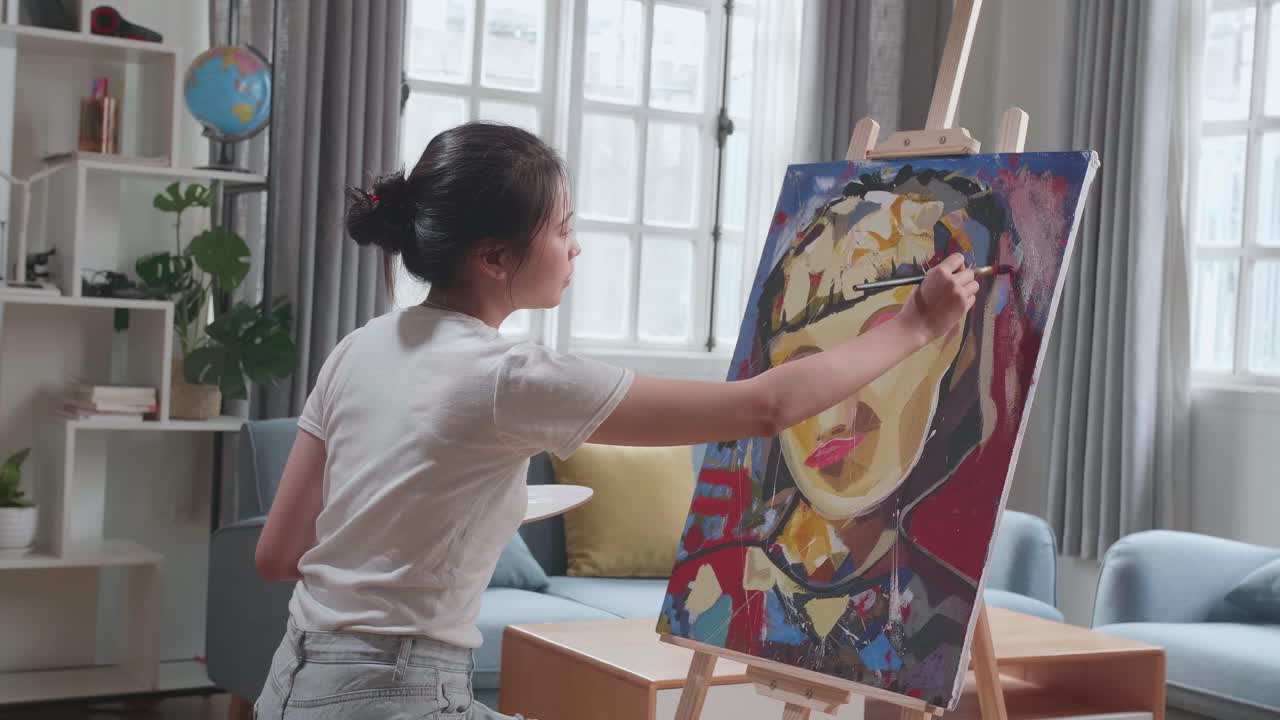 Medium Shot Of An Asian Artist Girl Coming To Sit Down And Holding Paintbrush Mixed Colour Before Painting A Girl'S Hair On The Canvas