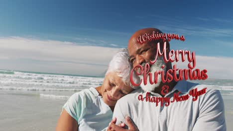 Animation-of-merry-christmas-over-happy-senior-biracial-couple-embracing-on-beach