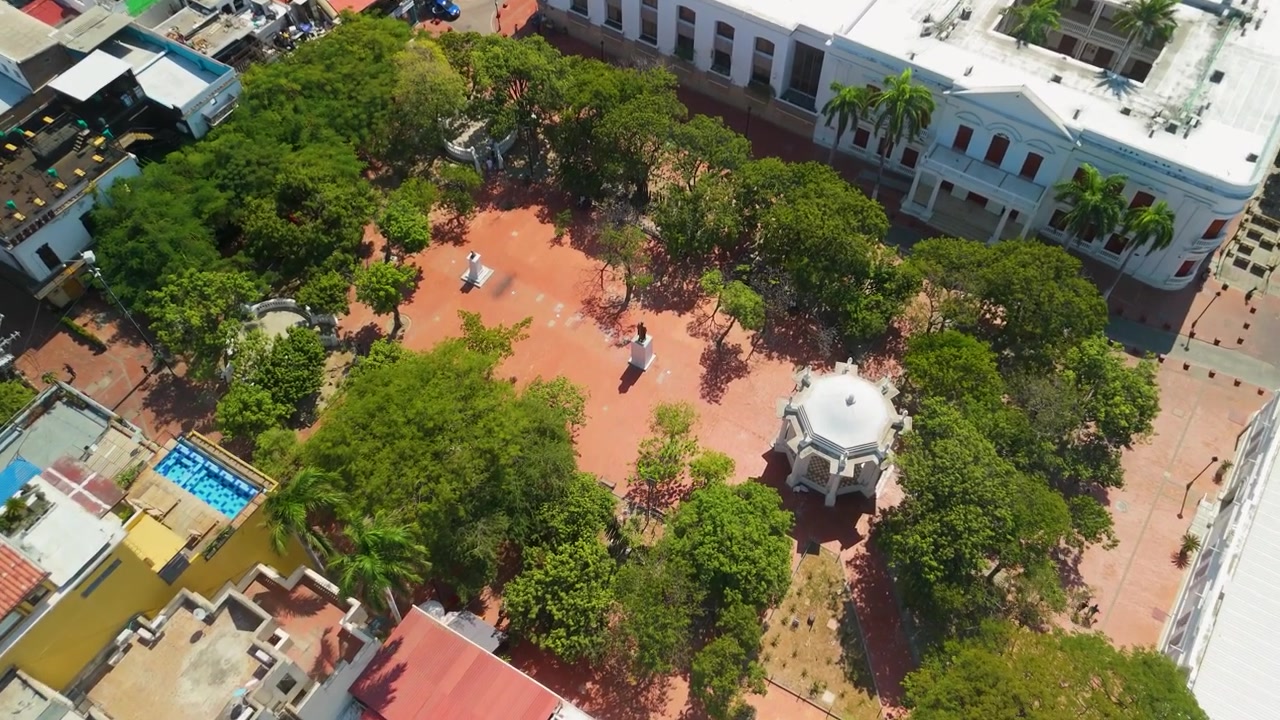Tarihi Santa Marta, Kolombiya'da yeşil ağaçlarla çevrili, beyaz çardaklı, Manuel Murillo Toro anıtı ve kırmızı tuğlalı meydana sahip Parque de Los Novios'a doğru havadan iniş.