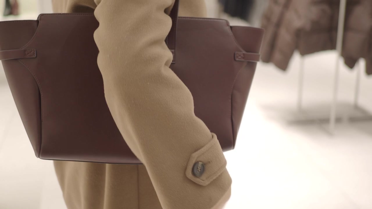 Donna con cappotto color cammello che porta una borsa tote in pelle marrone in un negozio