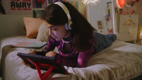 teenage girl relaxing with headphones and tablet in bedroom