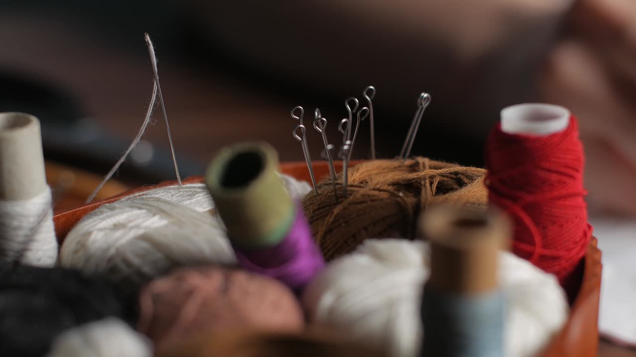 joven sastre fija piezas de textil blanco con alfileres de costura haciendo máscara facial reutilizable en el lugar de trabajo noche en casa. mano femenina tomando alfileres del hilo marrón. cerca