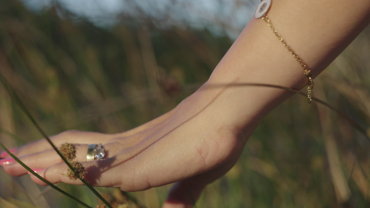 A woman's hand with pink nails gently caresses plants in a park in Spain