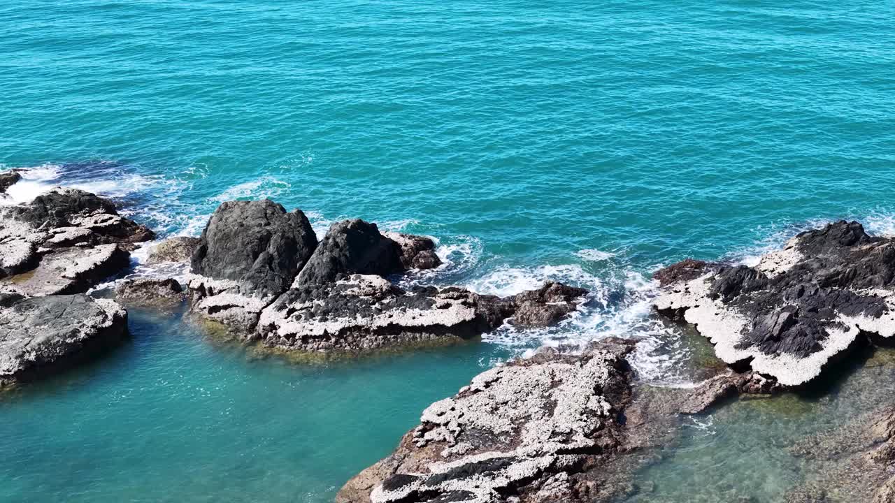 Aerial drone footage glides over turquoise coastal waters and rugged rocky outcrops near Port Douglas, with bright daylight and smooth camera movement