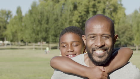 Father-carrying-his-son-on-his-back-while-walking-in-park.