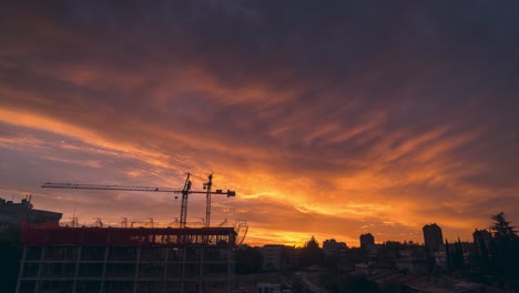 Vide-Ansicht-Im-Zeitraffer,-Spektakulärer-Und-Farbenfroher-Sonnenuntergang-Mit-Wolken-In-Einer-Stadt-Mit-Bauarbeiten-Wie-Kränen-Und-Gerüsten-Im-Vordergrund