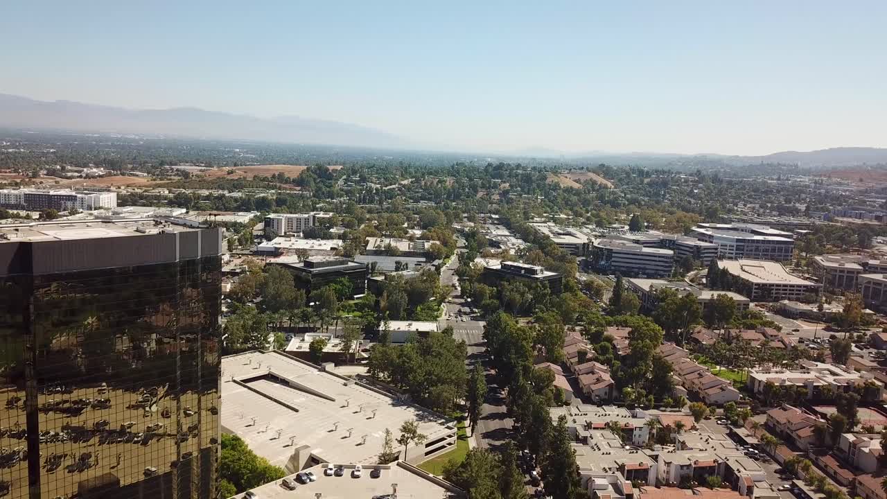 Aerial backwards shot of AIG Capital Service Building and parking cars in Woodland Hills, LA. Sunny day with main street and colorful trees in autumn.