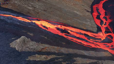 lava flow emerges from rock column and pours into a black volcanic landscape - aerial shot