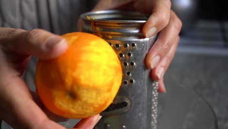 close-up person hand rubbing orange zest on a grater