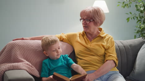 un niño divertido da vuelta las páginas del libro con la abuela en la sala de estar