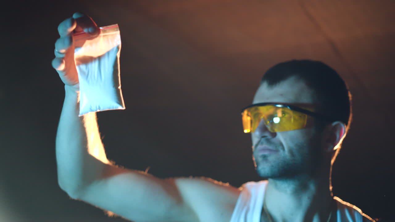 a gangster with glasses is examining the quality of the white powder in the basement. Illegal narcotics production