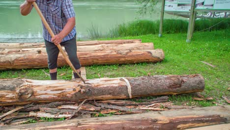 Man-uses-hand-tool-to-peel-or-remove-bark-from-a-log-near-river