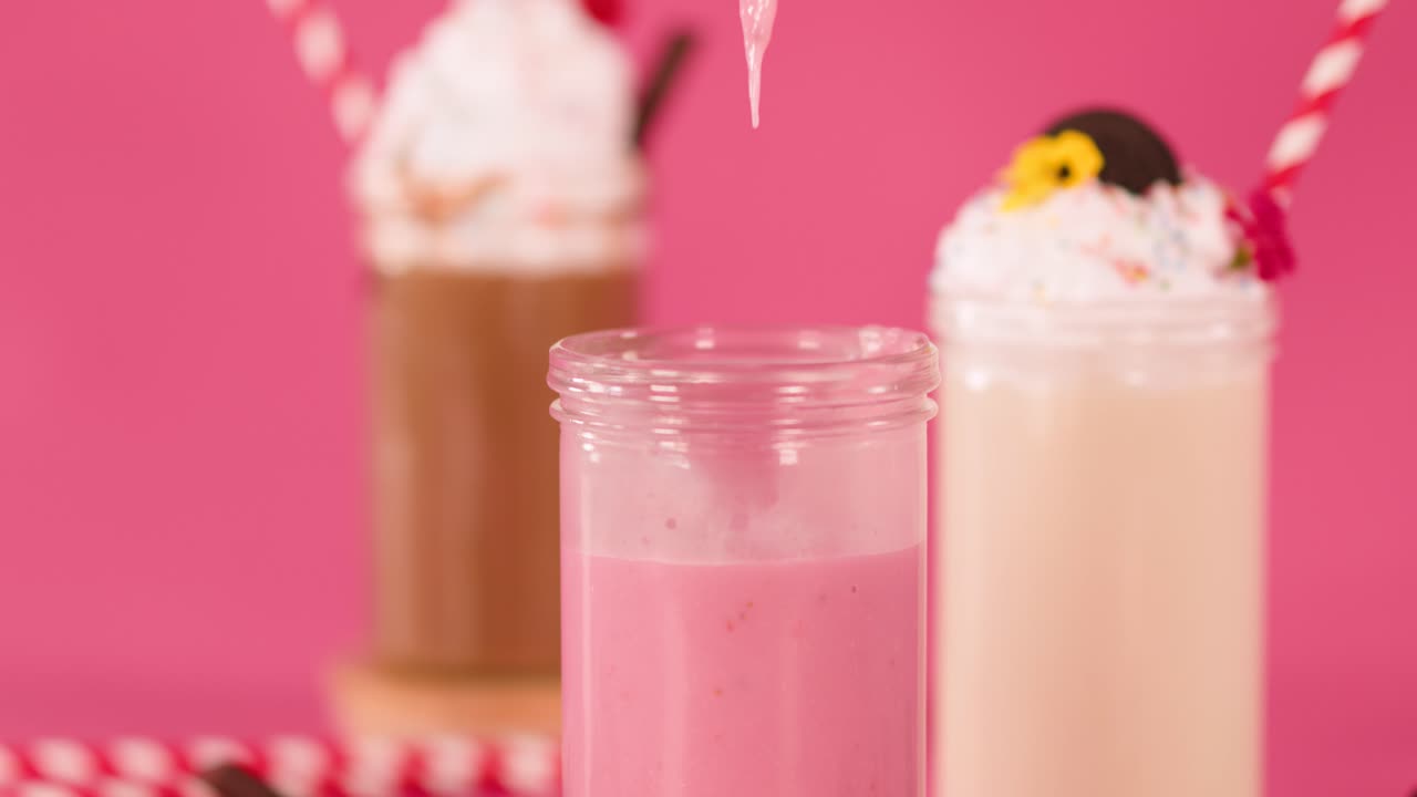 Strawberry milkshake poured into glass, colorful background, bright lighting, close-up, dessert drinks