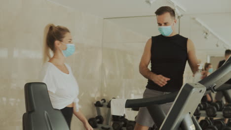 giovane atleta femminile e maschile con maschera facciale utilizzando disinfettante per le mani e macchine per esercizi in palestra