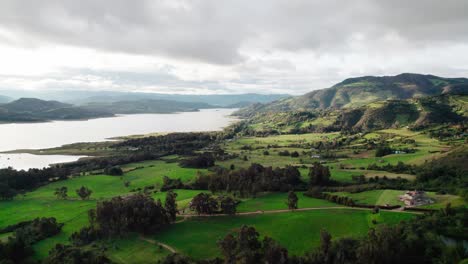 Drone zoom in view of Guatavita valley with lush fields, trees and distant mountains in Colombia