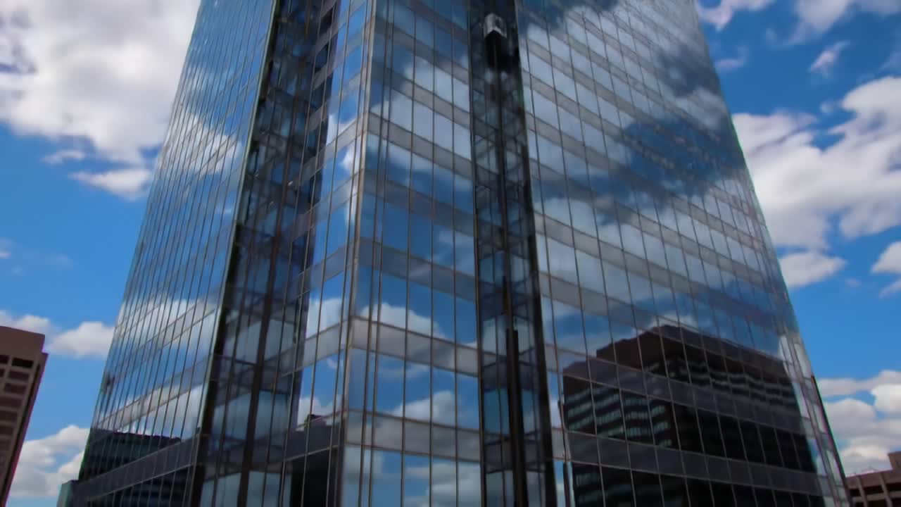 A Stunning Skyscraper Shines Under a Clear Blue Sky, Reflecting Cloud Patterns and Surrounding Urban Architecture in This Impressive Modern Cityscape