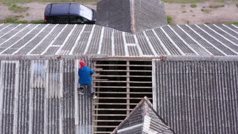 Contractor-scales-exposed-gable-and-valley-roof-frame,-barn-ridge-aerial-pan-up