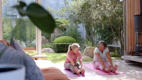 stretching on yoga mats, multiracial female friends exercising together in garden