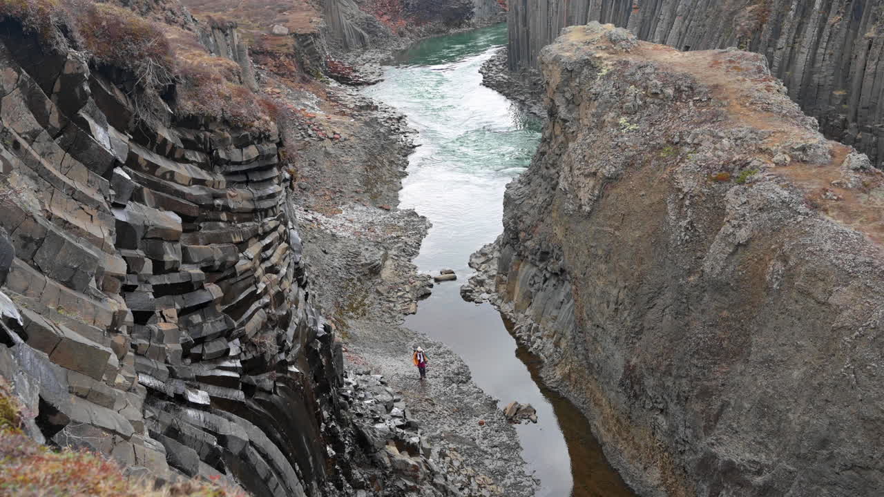 회색 현무암 기둥이 있는 협곡에서 강가를 걷는 사람
