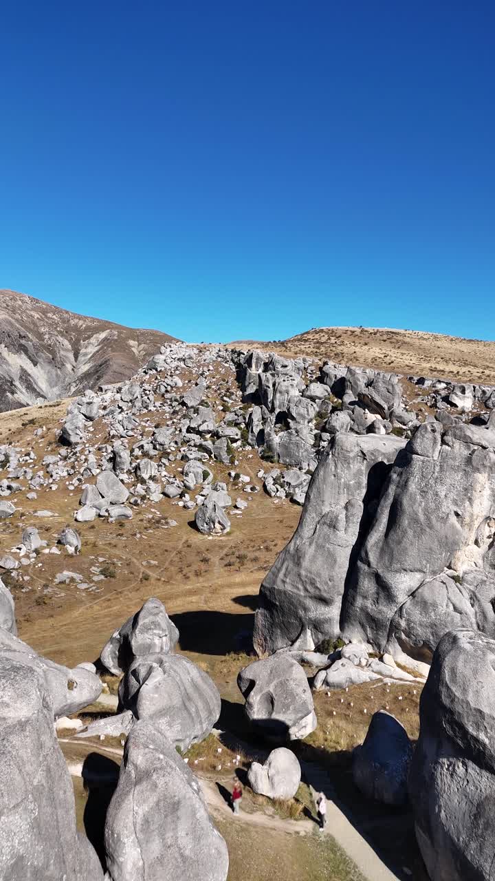 Close vertical drone flyover of rocky outcrops at Castle Hill under bright midday light, dolly passing hikers below