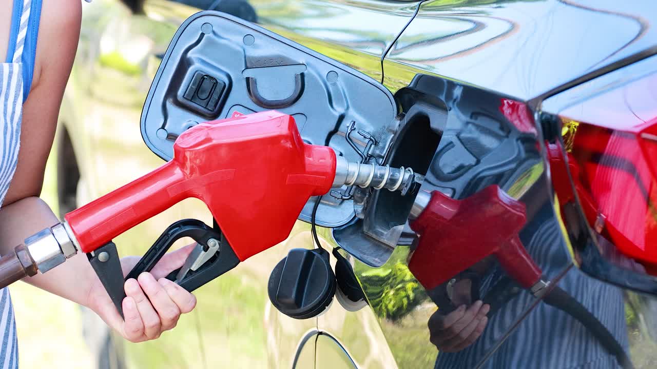 Person refueling vehicle with gasoline pump nozzle outdoors, bright daylight, close-up perspective