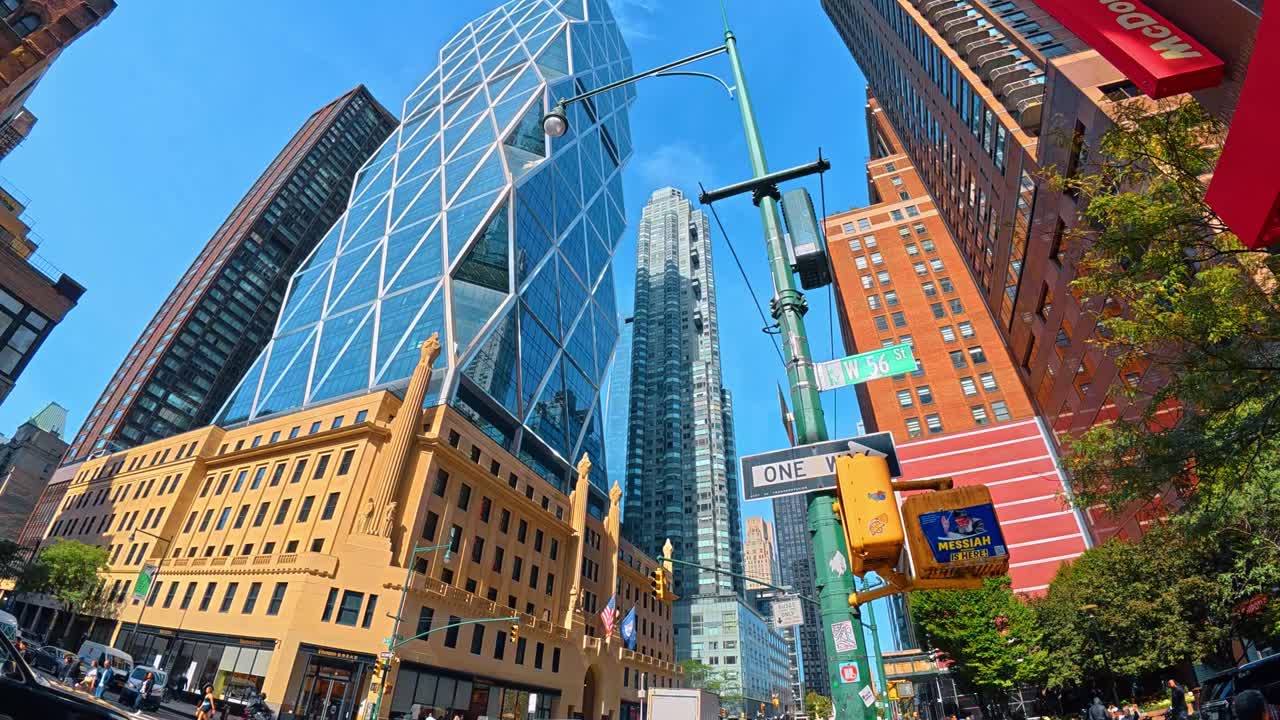 New York, USA, 7 agosto 2025: Prospettiva della facciata in vetro della Hearst Tower e dei cartelli stradali. Vista verso l'alto dell'architettura in vetro della Hearst Tower con i cartelli stradali di Midtown Manhattan e il cielo blu.